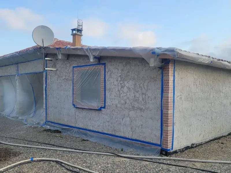 Maison de plain-pied à l’ancien crépi gris, menuiseries protégées avant la projection