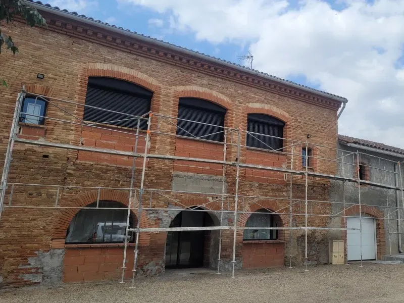 Façade en brique d’un corps de ferme sous échafaudage, avant le ravalement